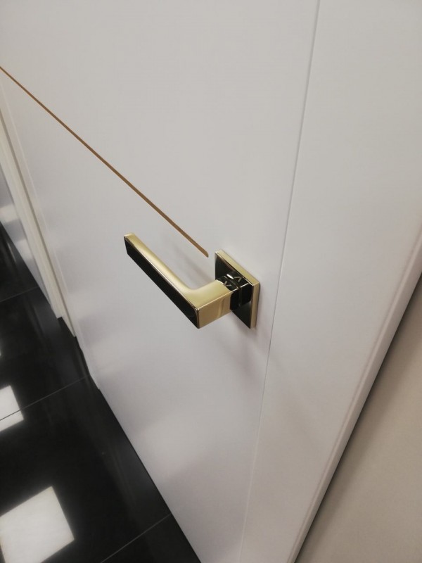 Muy bonita instalación del tirador Warna en color dorado sobre una puerta blanca con un motivo dorado